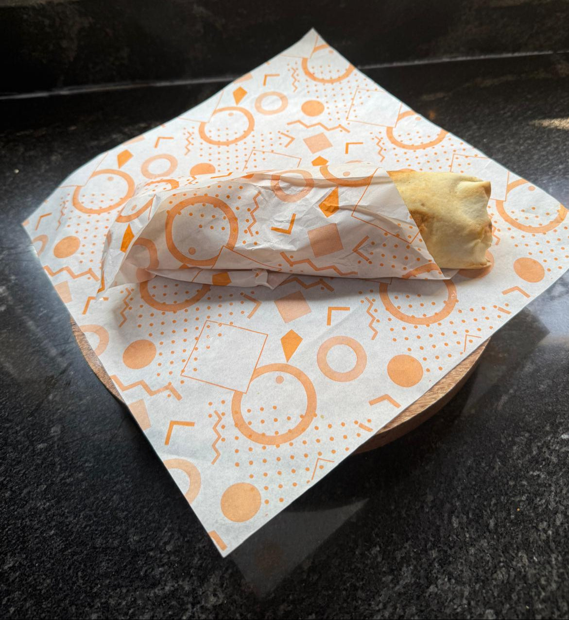 Burrito / Shawarma wrapped in orange grease paper on a patterned napkin 